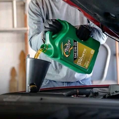 Person pouring oil from a green container into a funnel under a car hood.