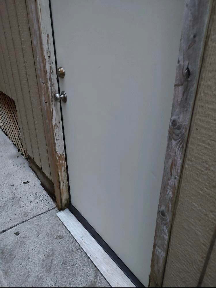 A white door is sitting on a sidewalk next to a wooden wall.