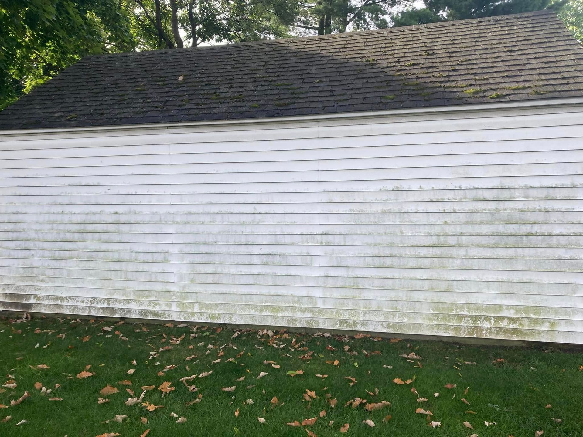 A white building with a black roof is sitting on top of a lush green field.