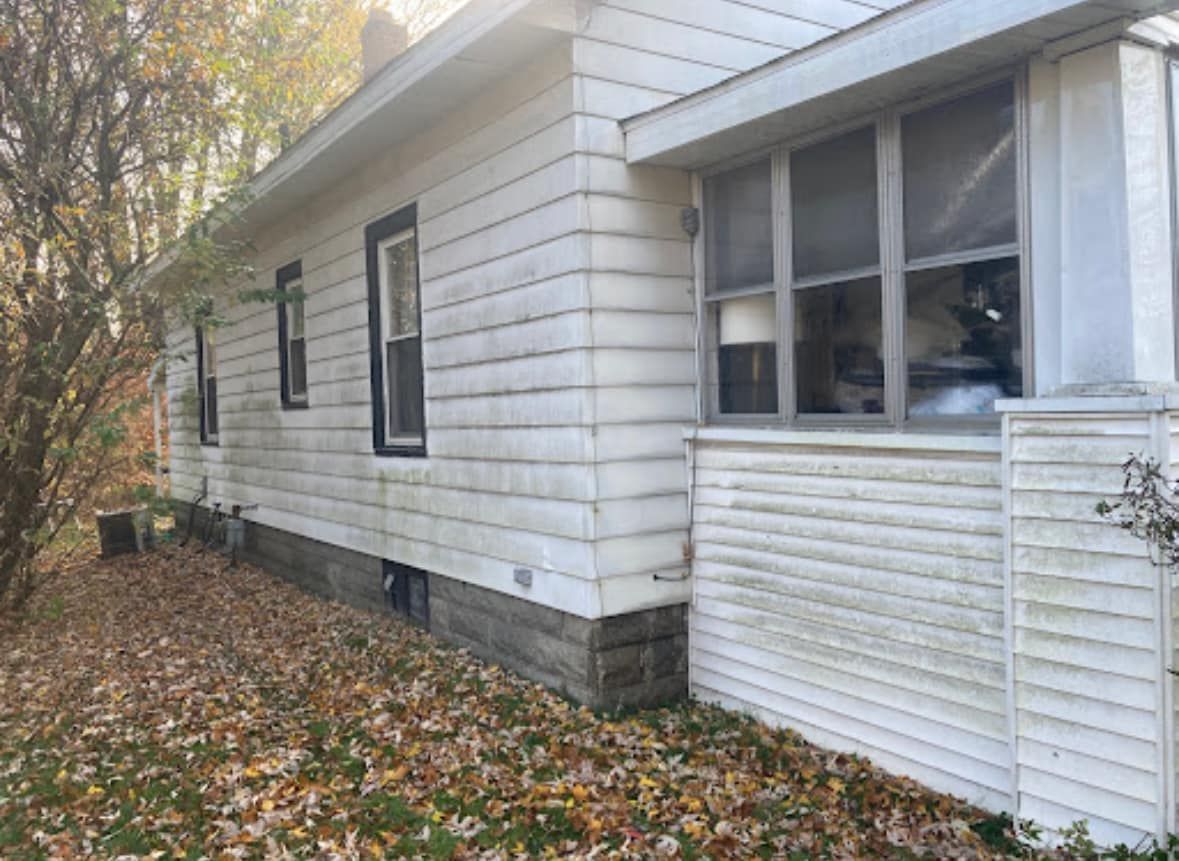 A white house with a lot of windows and leaves on the ground.