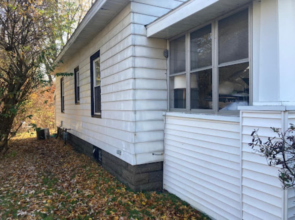 A white house with a lot of windows and leaves on the ground.