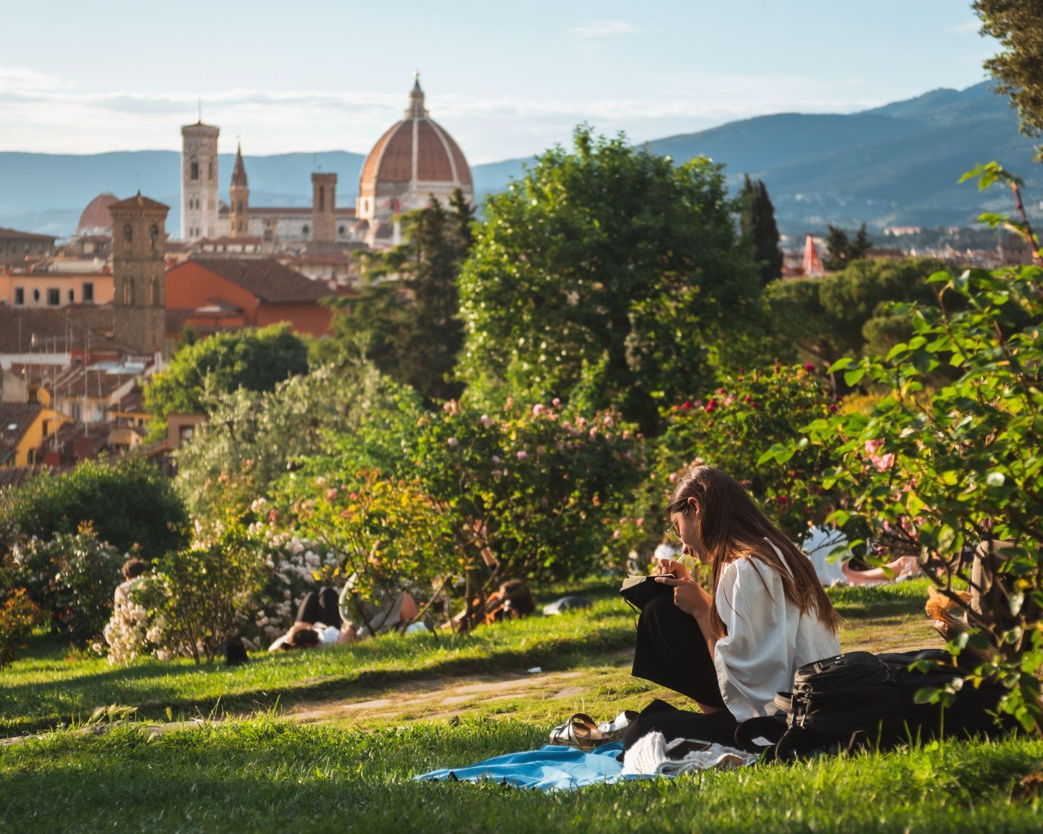 Woman eating outdoors with Florence's Duomo in the background. Lush greenery, blue sky.