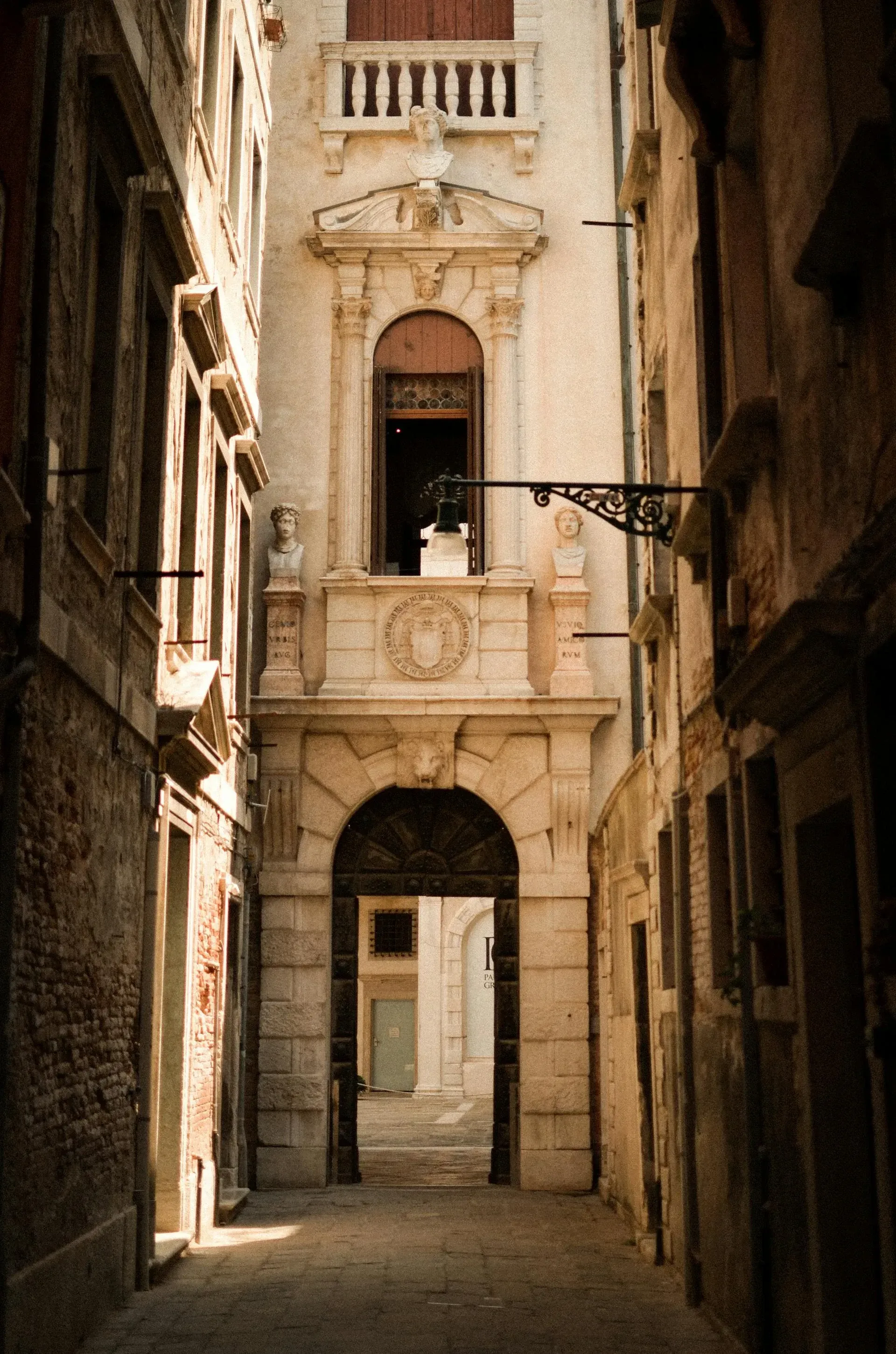 Narrow, sunlit alley in Venice, Italy, with a white, ornate building facade at the end.