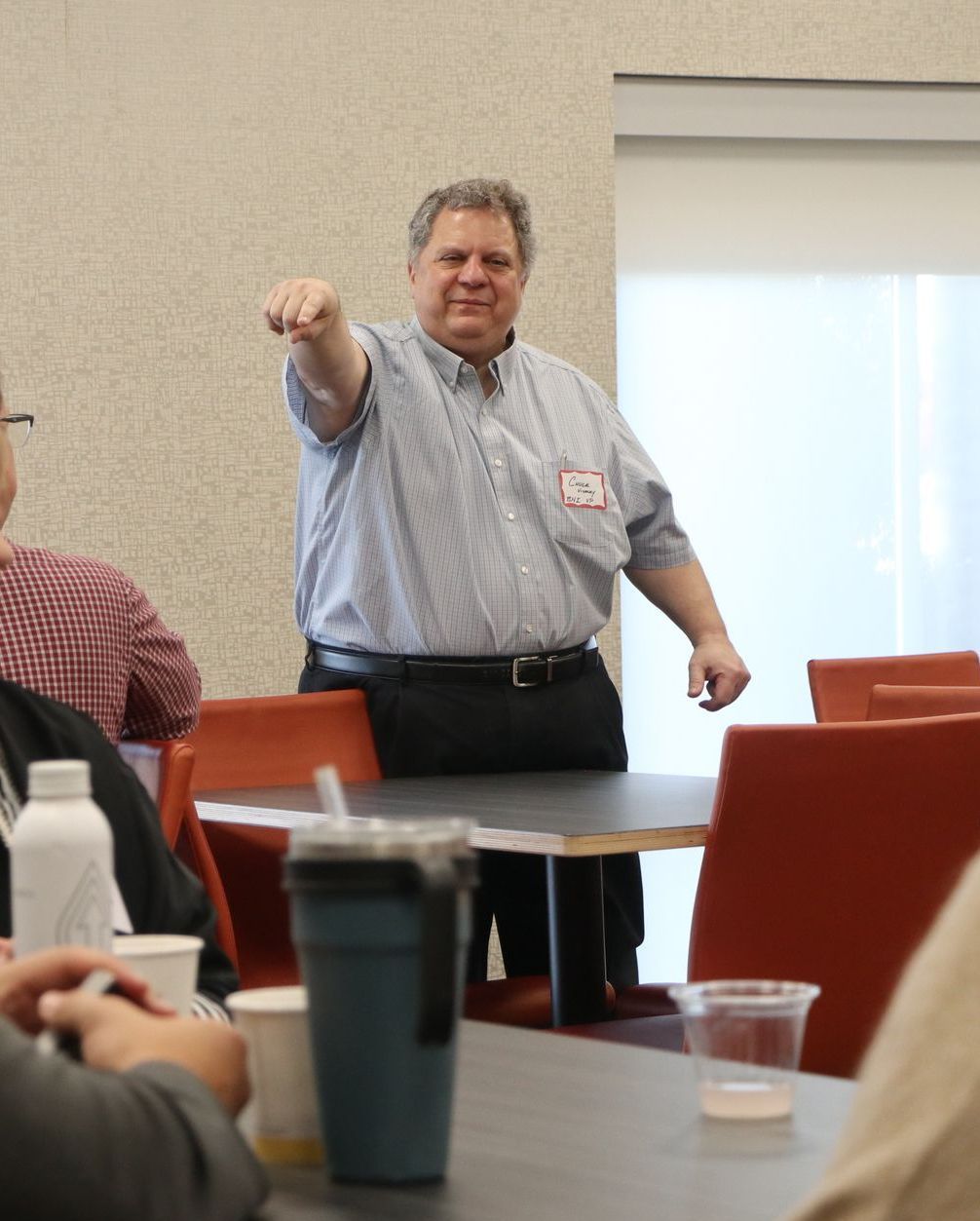 A man wearing a name tag stands in front of a group of people
