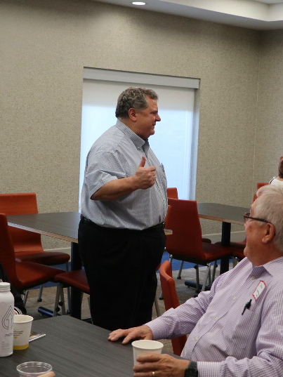 A man wearing a name tag stands in front of a group of people