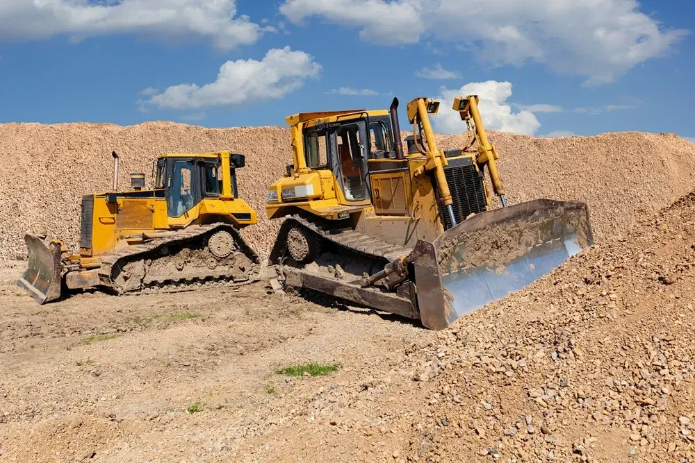 Two yellow bulldozers on a dirt lot, pushing mounds of gravel under a blue sky. — Shantui QLD in Warwick, QLD