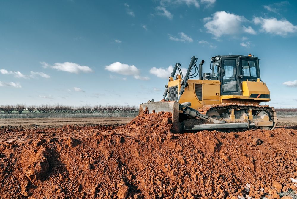 Yellow bulldozer pushing reddish-brown dirt on construction site under a blue sky — Shantui QLD in Goondiwindi, QLD
