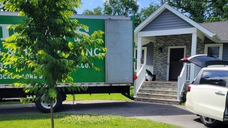 A green moving truck is parked in front of a house.