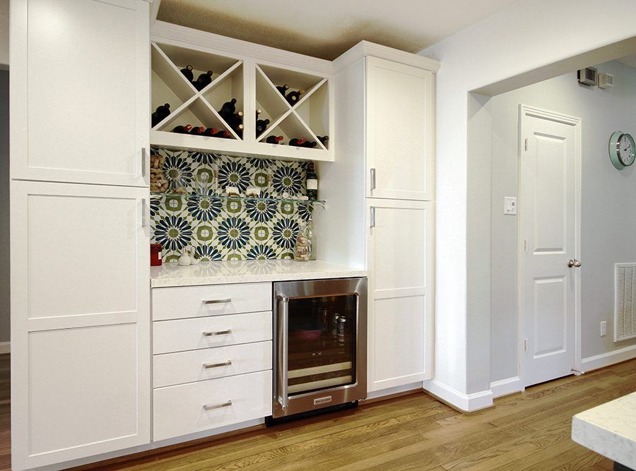 White kitchen with tiled backsplash, wine rack, built-in oven, and hardwood floor.