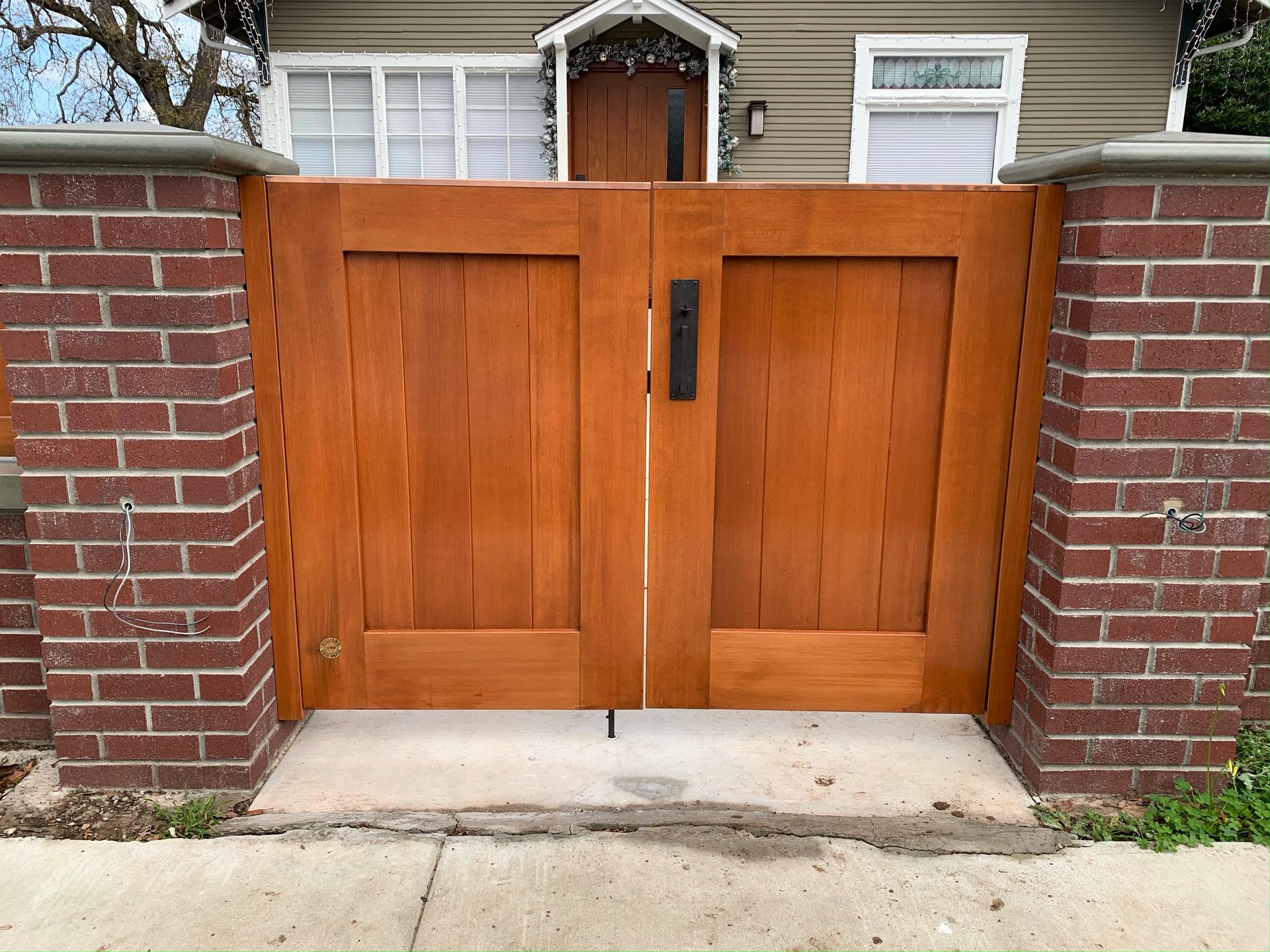 A wooden gate is between two brick pillars in front of a house