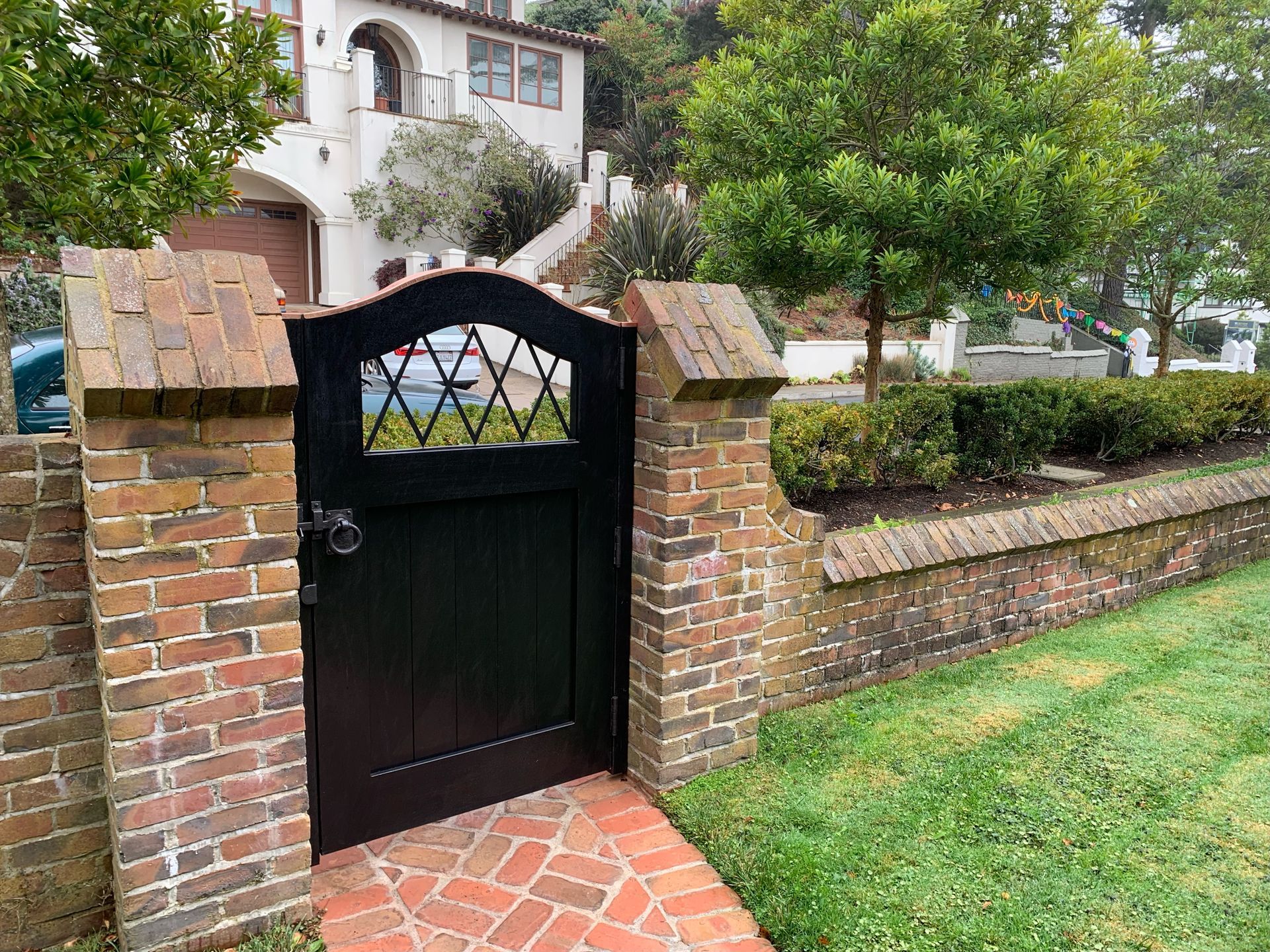 A black gate is surrounded by a brick wall in front of a house.