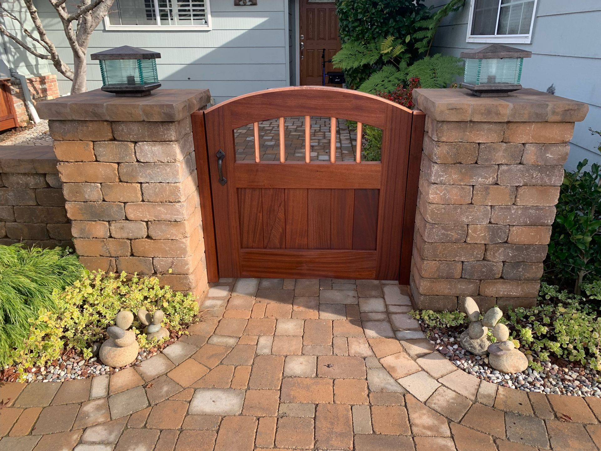 A wooden gate is surrounded by brick pillars in front of a house.