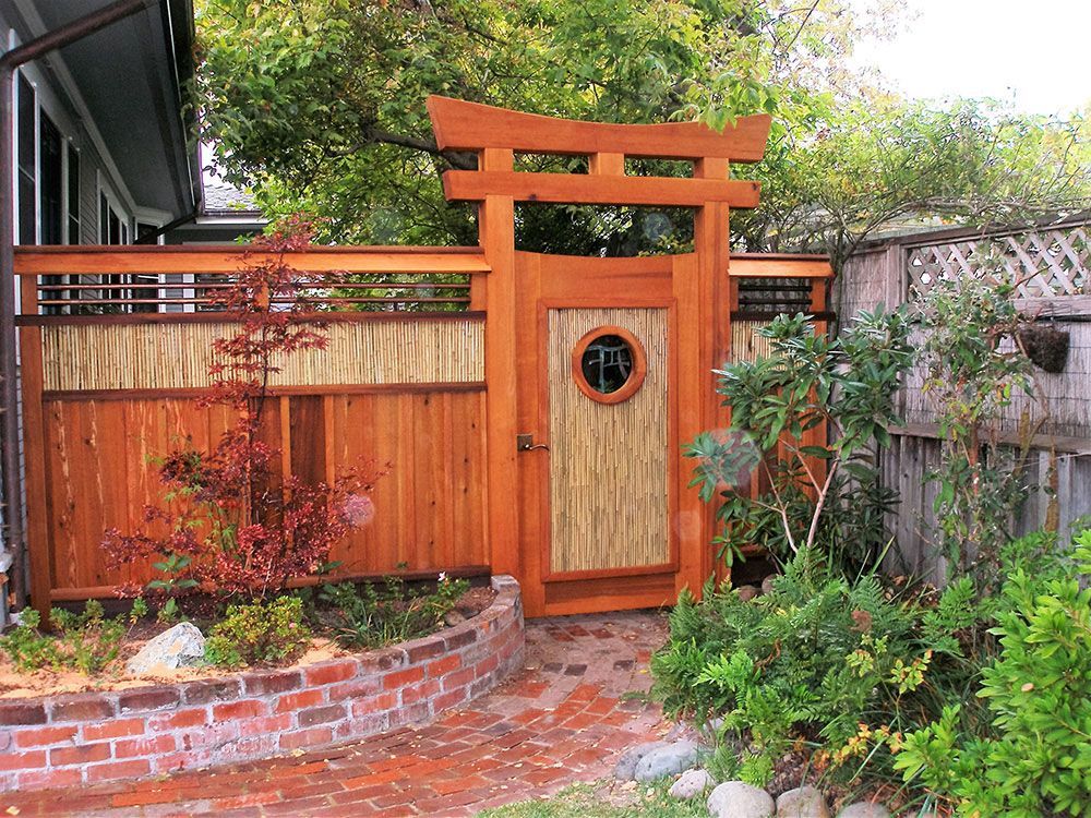 A wooden gate with a round window is in a garden.