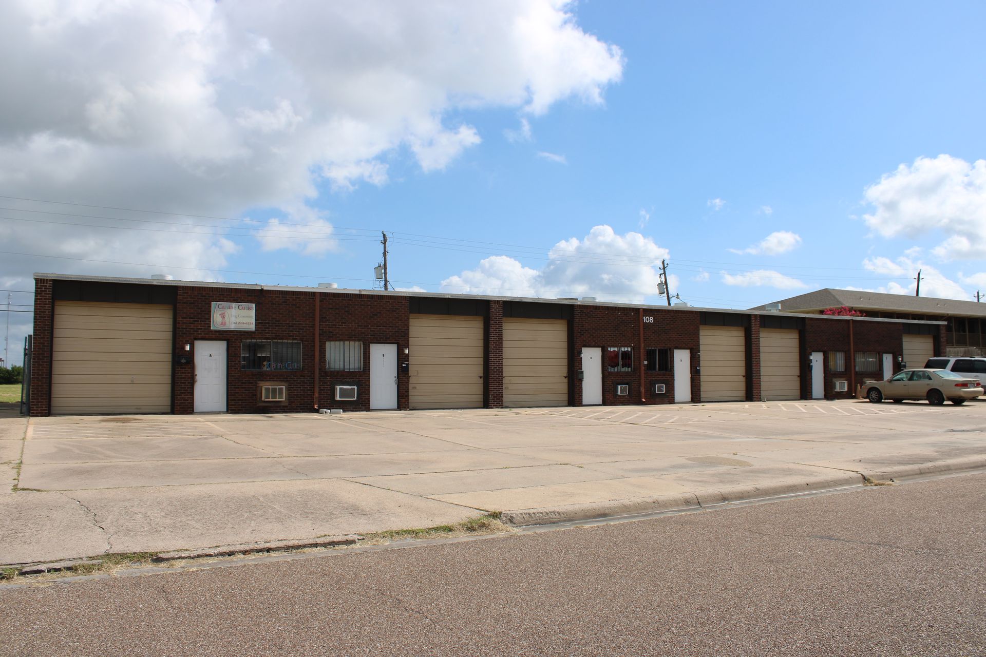 Brick building with multiple garage doors, white doors, and cars parked in front.