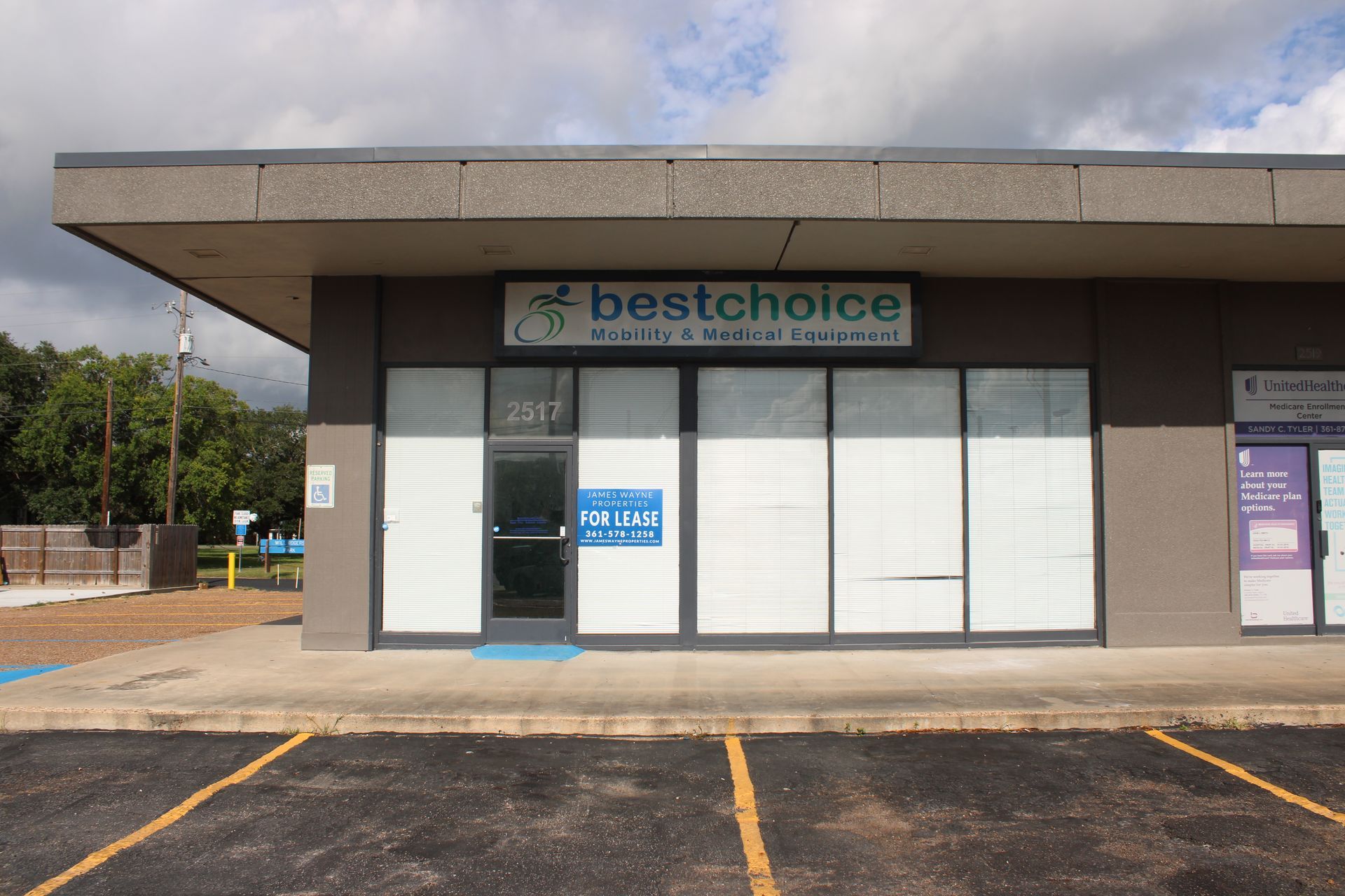 Exterior of "Best Choice" store with "For Lease" sign. Grey building, glass windows, blue door.