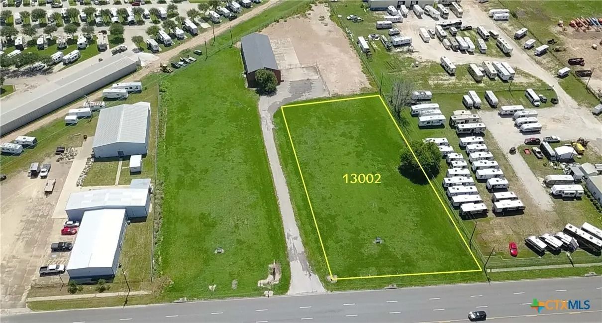 Aerial view of a grassy lot outlined in yellow with nearby buildings and RVs; a road is in the foreground.