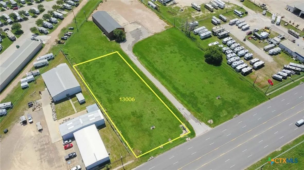 Aerial view of a grassy lot bordered by yellow lines, surrounded by buildings, vehicles, and a highway.