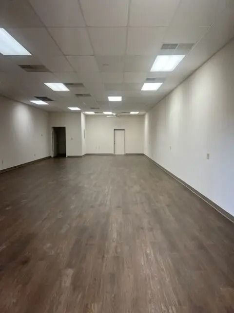 Empty room with wood-look flooring, white walls, and recessed ceiling lights. Two doorways are visible.