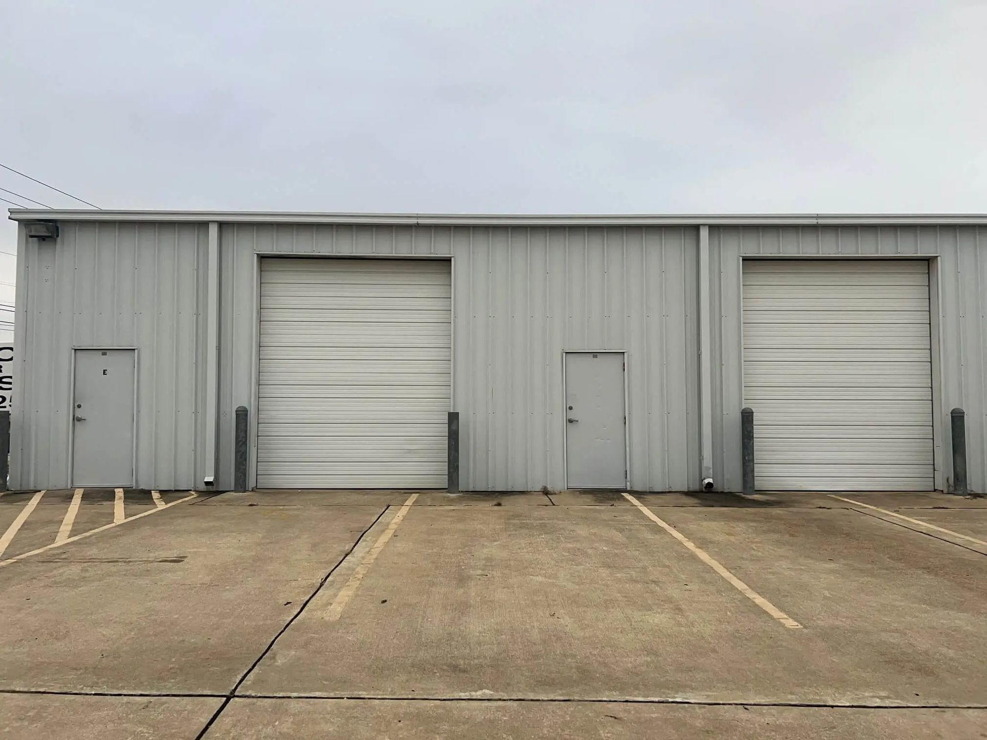 Gray metal building with three doors: two garage doors and one pedestrian door, with parking spaces in front.