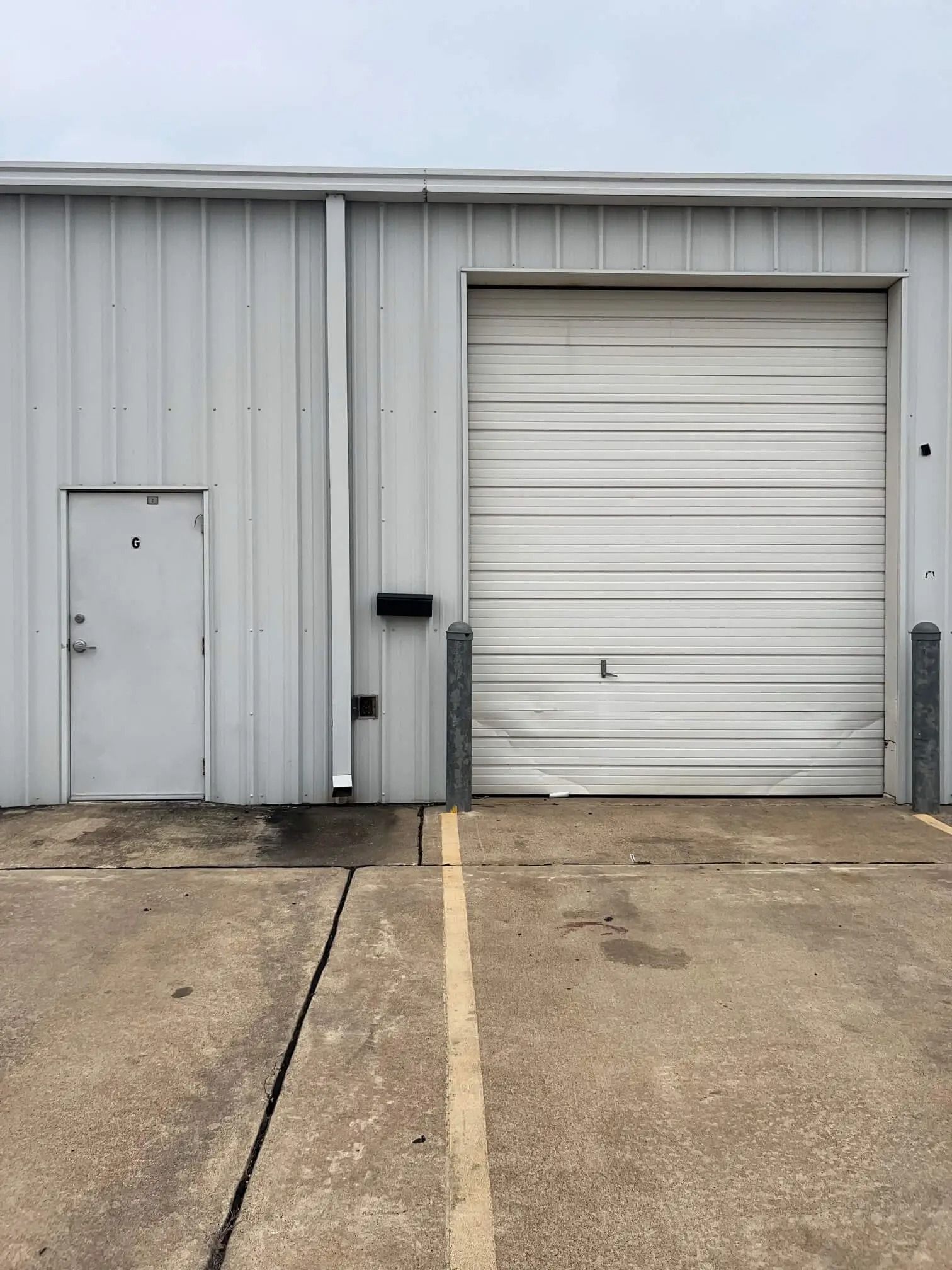 Exterior of a light gray industrial building with a closed garage door, a small door with the number 4, and a concrete parking area.
