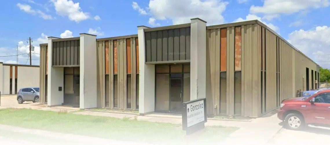 A mid-century modern style commercial building with beige walls and a blue sky background. A red SUV and a gray SUV are parked in front.