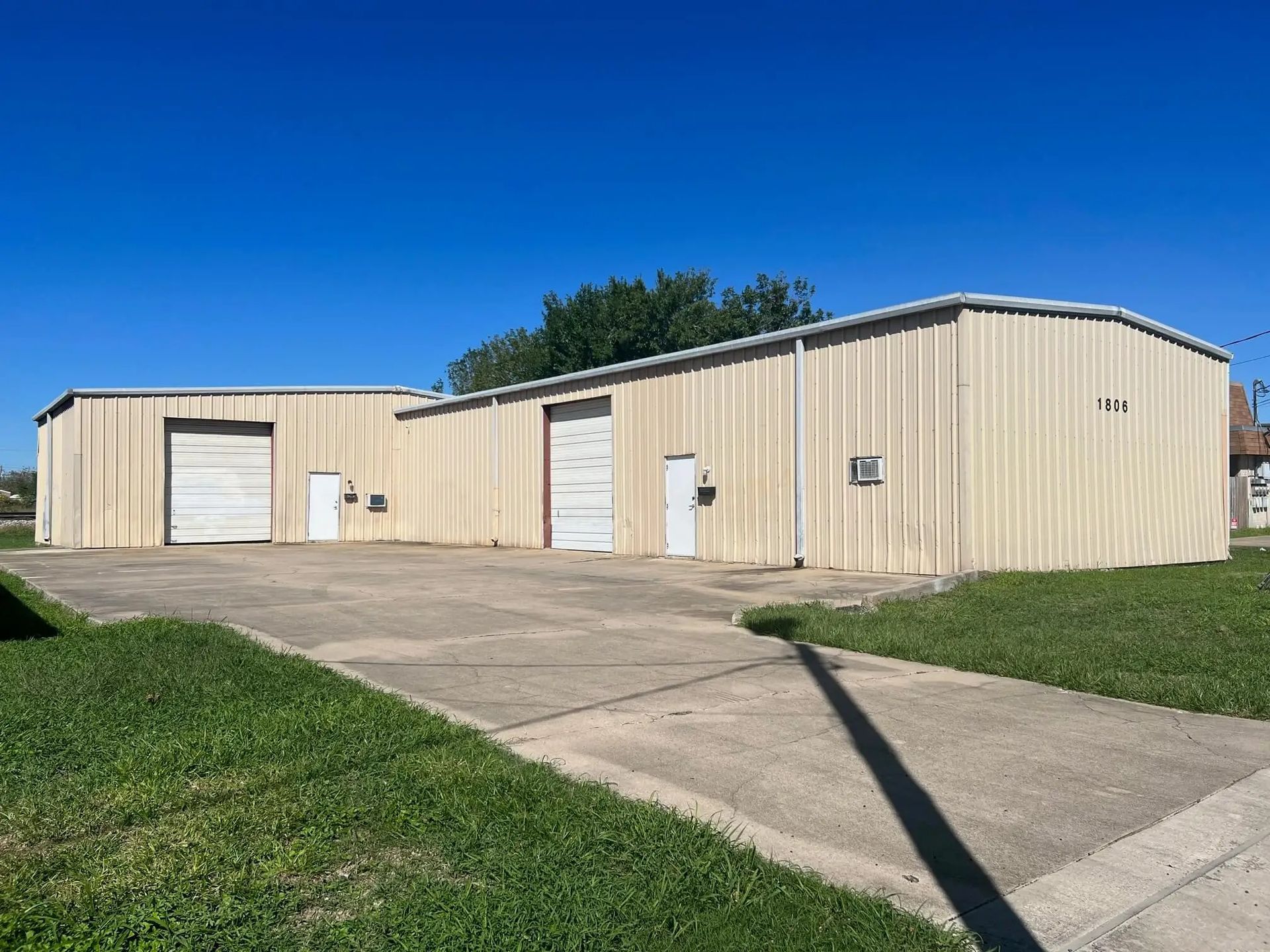 Exterior of a commercial building with two garage doors and a concrete driveway, set on a grassy lot under a blue sky.