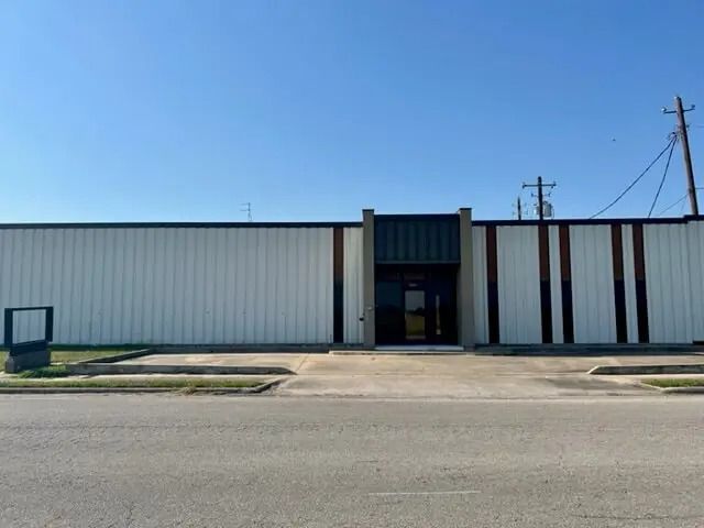 A commercial building with a white exterior, a recessed dark entry, and vertical brown accents on a sunny day.