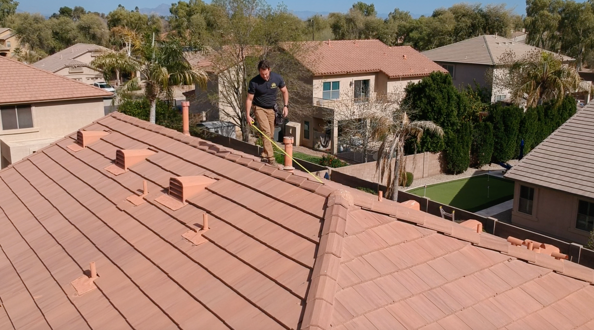 A man standing on top of a roof with a tape measure