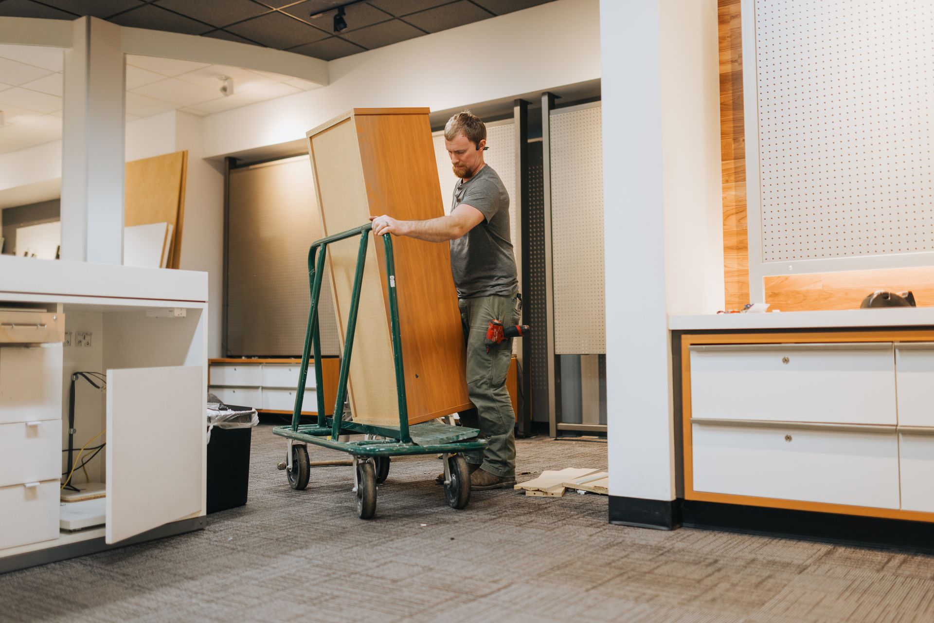 A man is pushing a cart with a piece of wood on it.