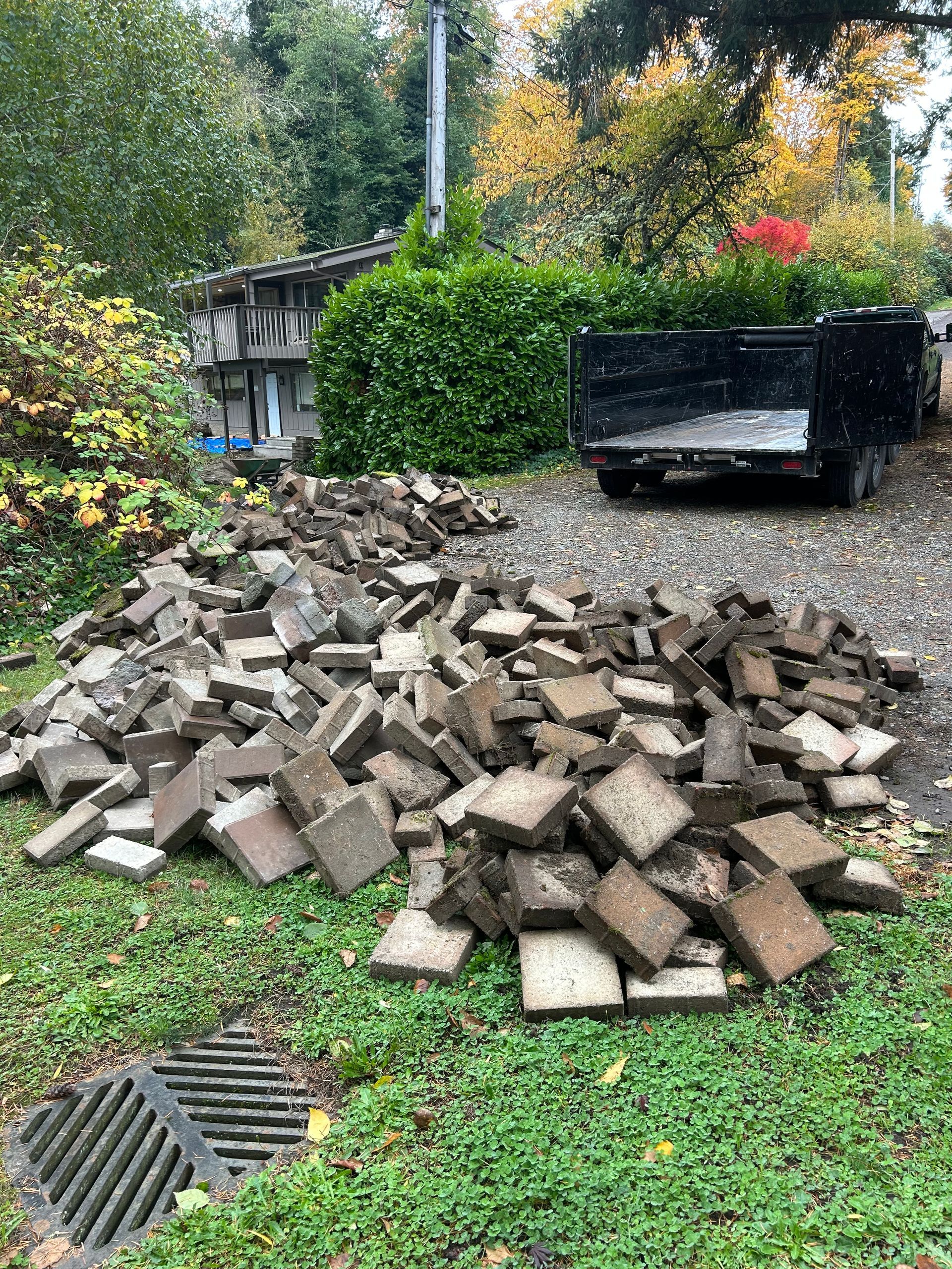 Pile of broken bricks going to recycle, near a parked trailer and building. Drain grate in foreground.