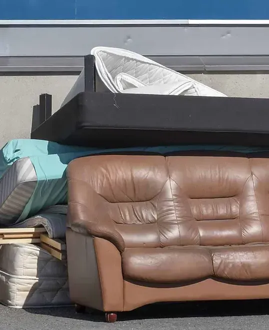 A brown leather couch is sitting next to a pile of mattresses.
