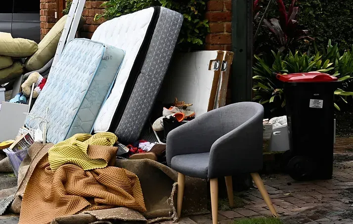 A pile of furniture is sitting on the sidewalk in front of a house.