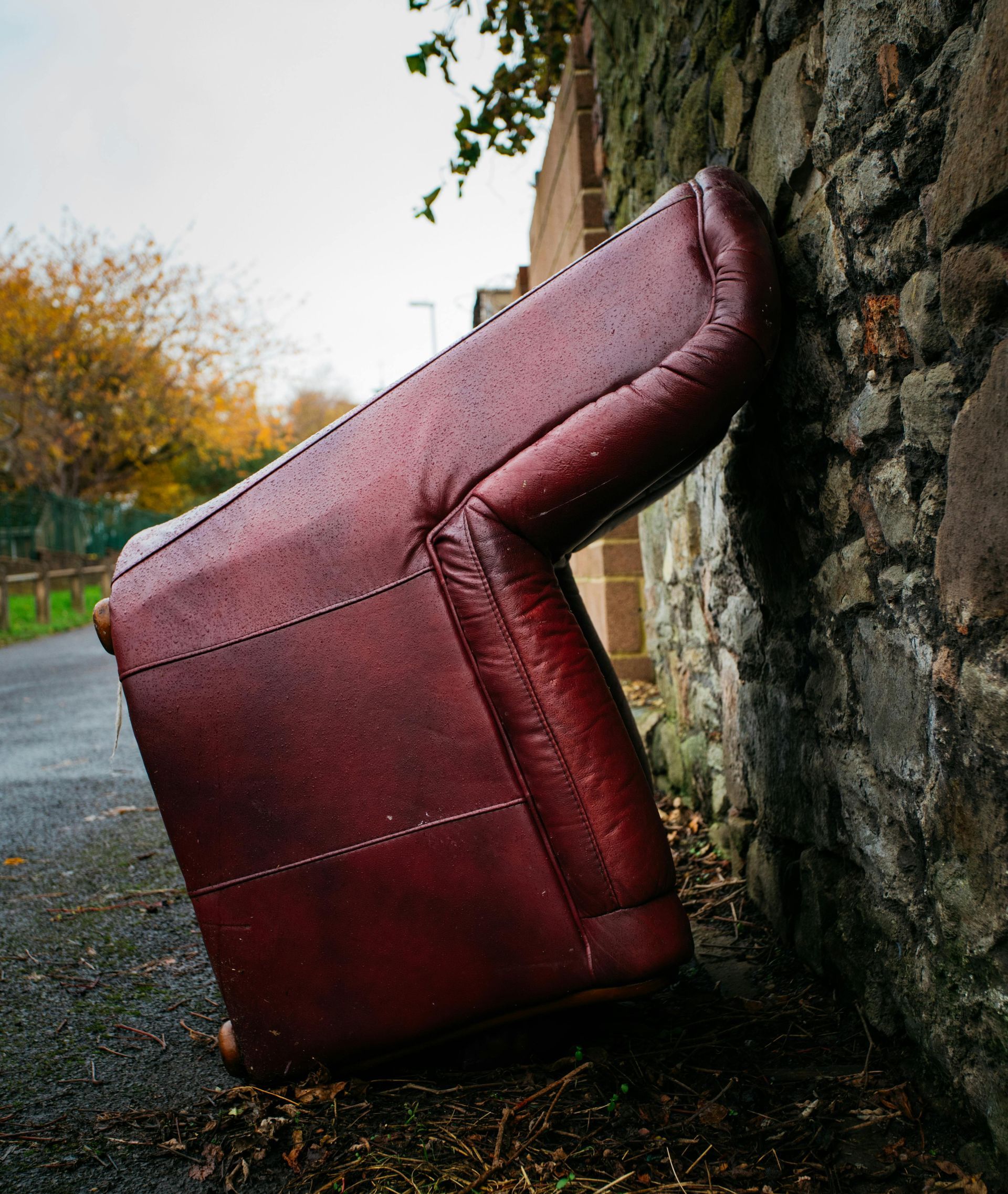 A red leather couch is leaning against a stone wall.