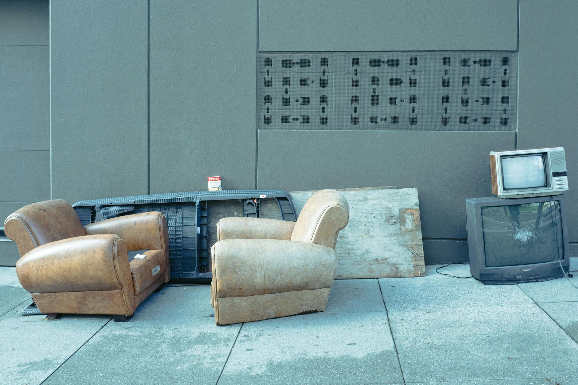 Two chairs and a television are sitting on the sidewalk in front of a building.