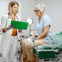 Doctor in lab coat consults elderly woman during exam in an office.