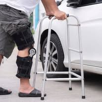 Person with leg brace uses walker near a car.