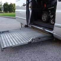Silver van with a wheelchair ramp extended, ready for access.