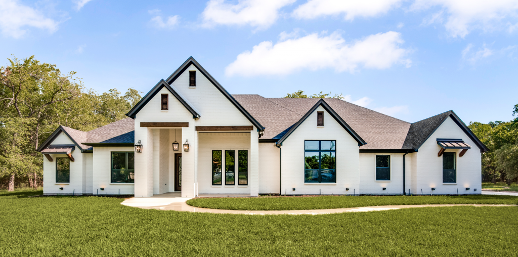 A large white house with black trim is sitting on top of a lush green lawn.