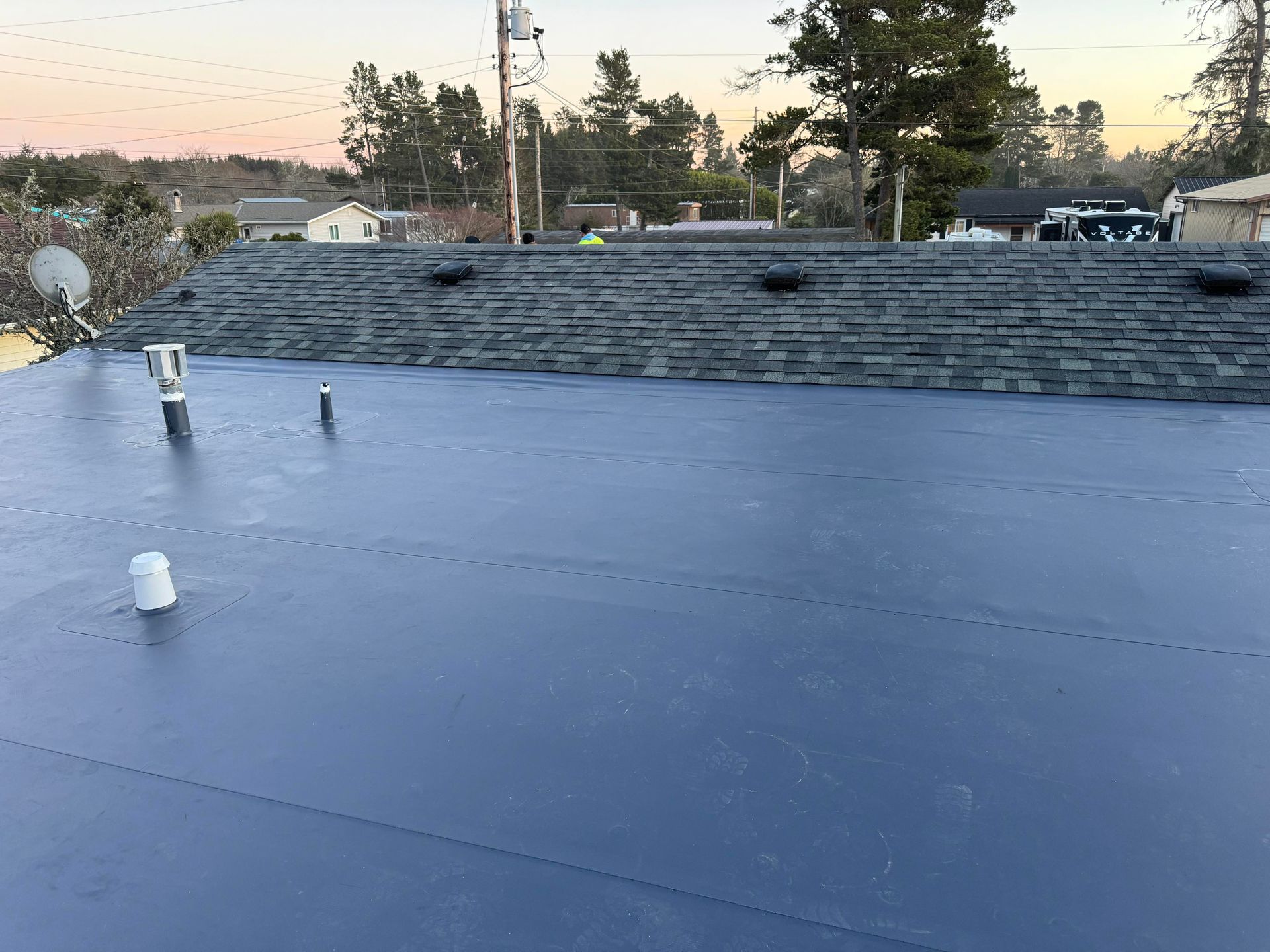 Flat blue roof with vents and a low stone wall at sunset.