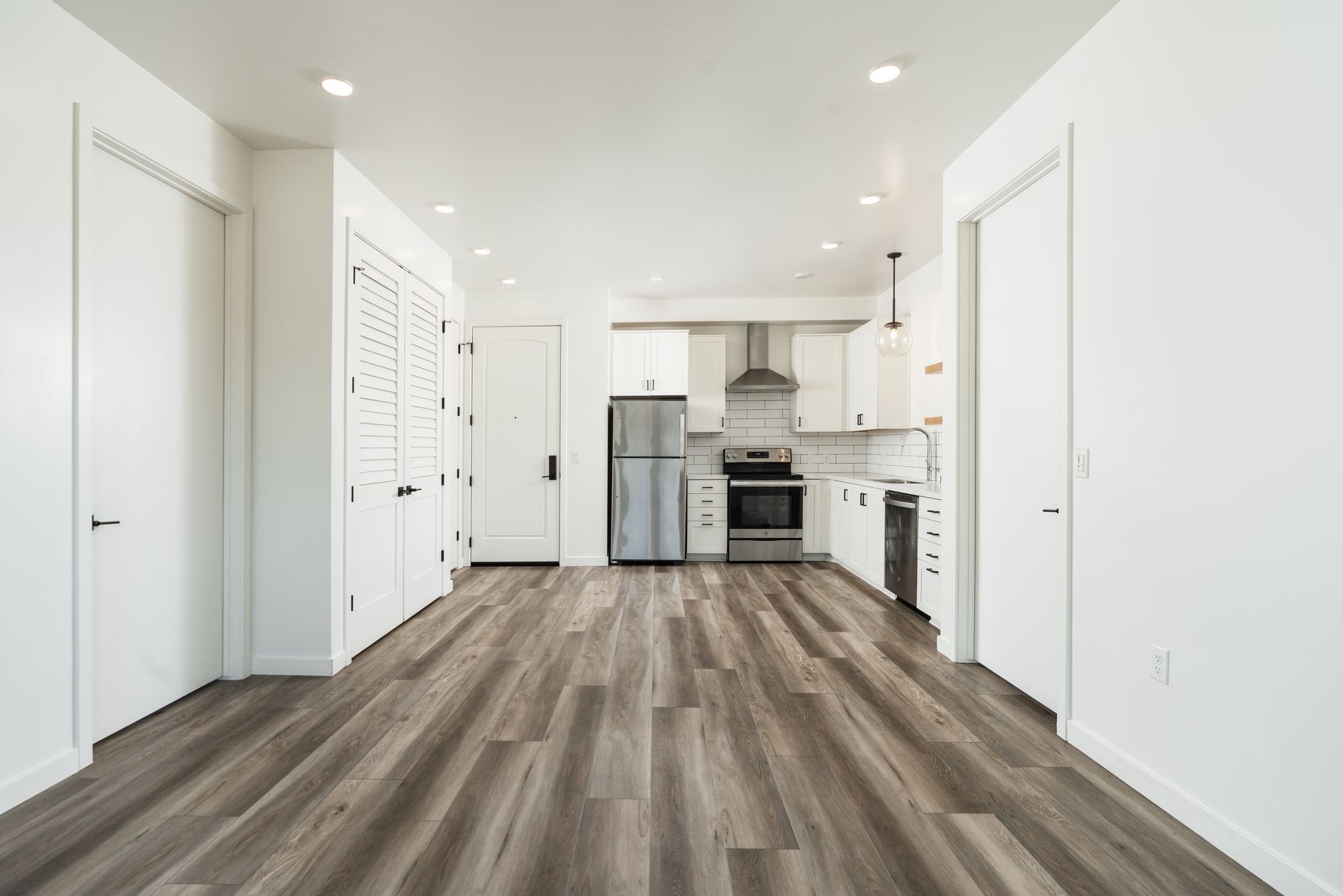 An empty kitchen with hardwood floors and white cabinets.