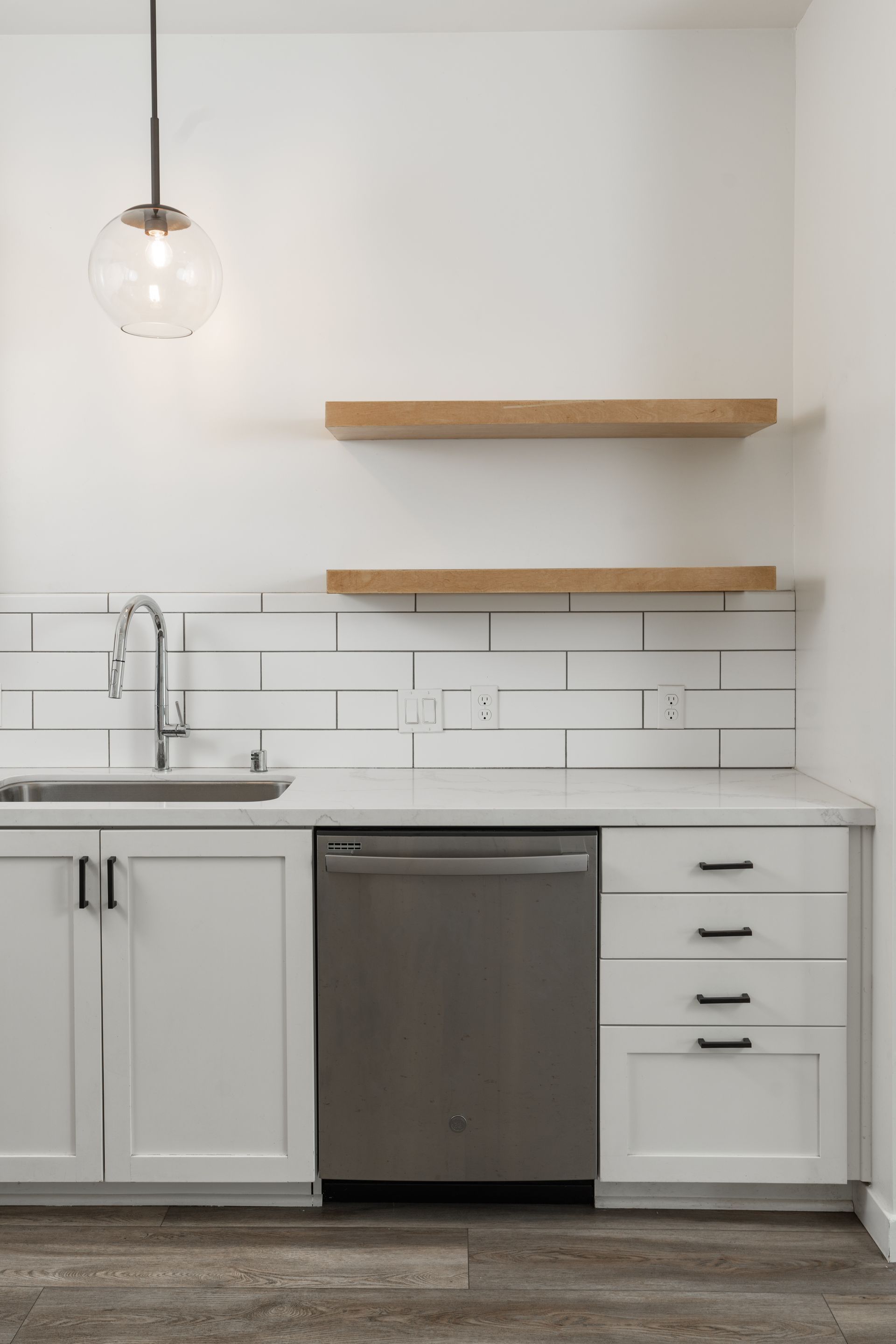 A kitchen with white cabinets , a sink , and a stainless steel dishwasher.