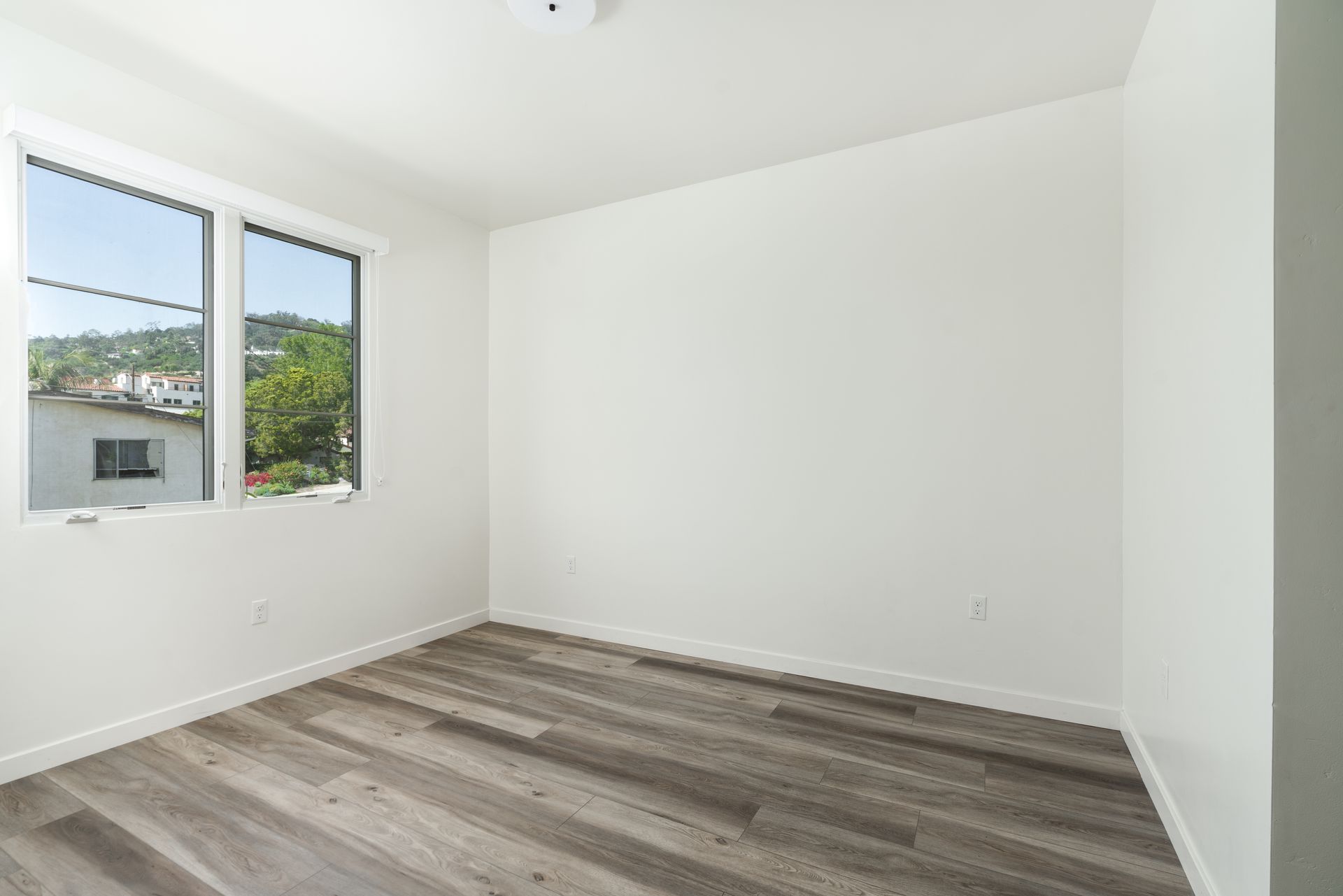 An empty room with a wooden floor and two windows.