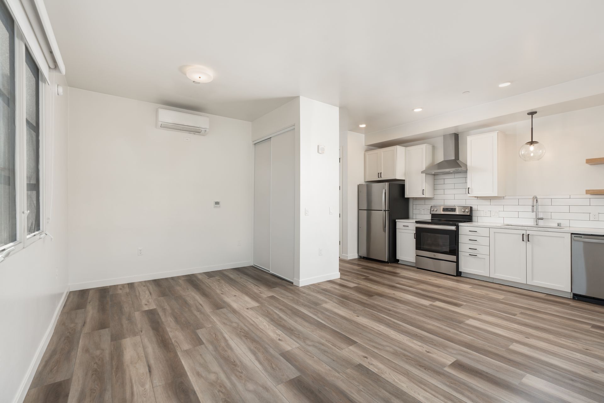 A living room with hardwood floors and a kitchen with stainless steel appliances.