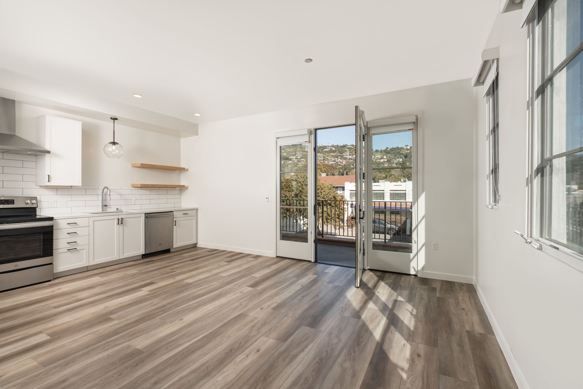 A living room with hardwood floors and a kitchen with stainless steel appliances.