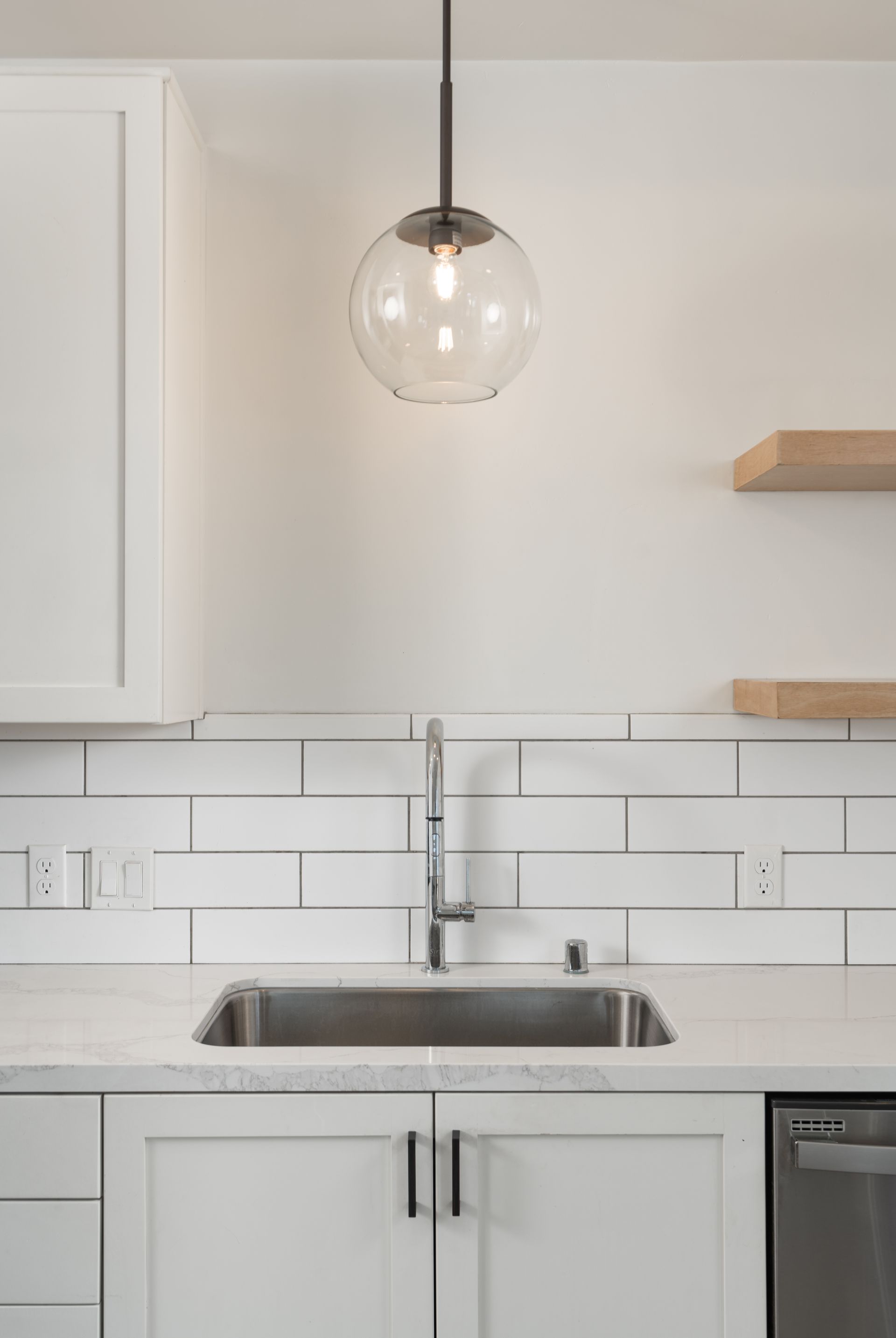 A kitchen with white cabinets , a sink , and a light hanging from the ceiling.