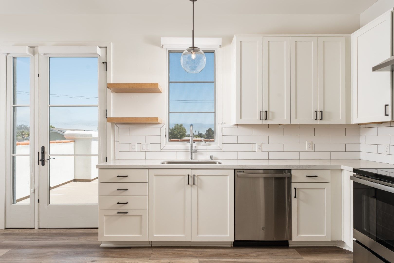 A kitchen with white cabinets , stainless steel appliances , a sink , and a window.