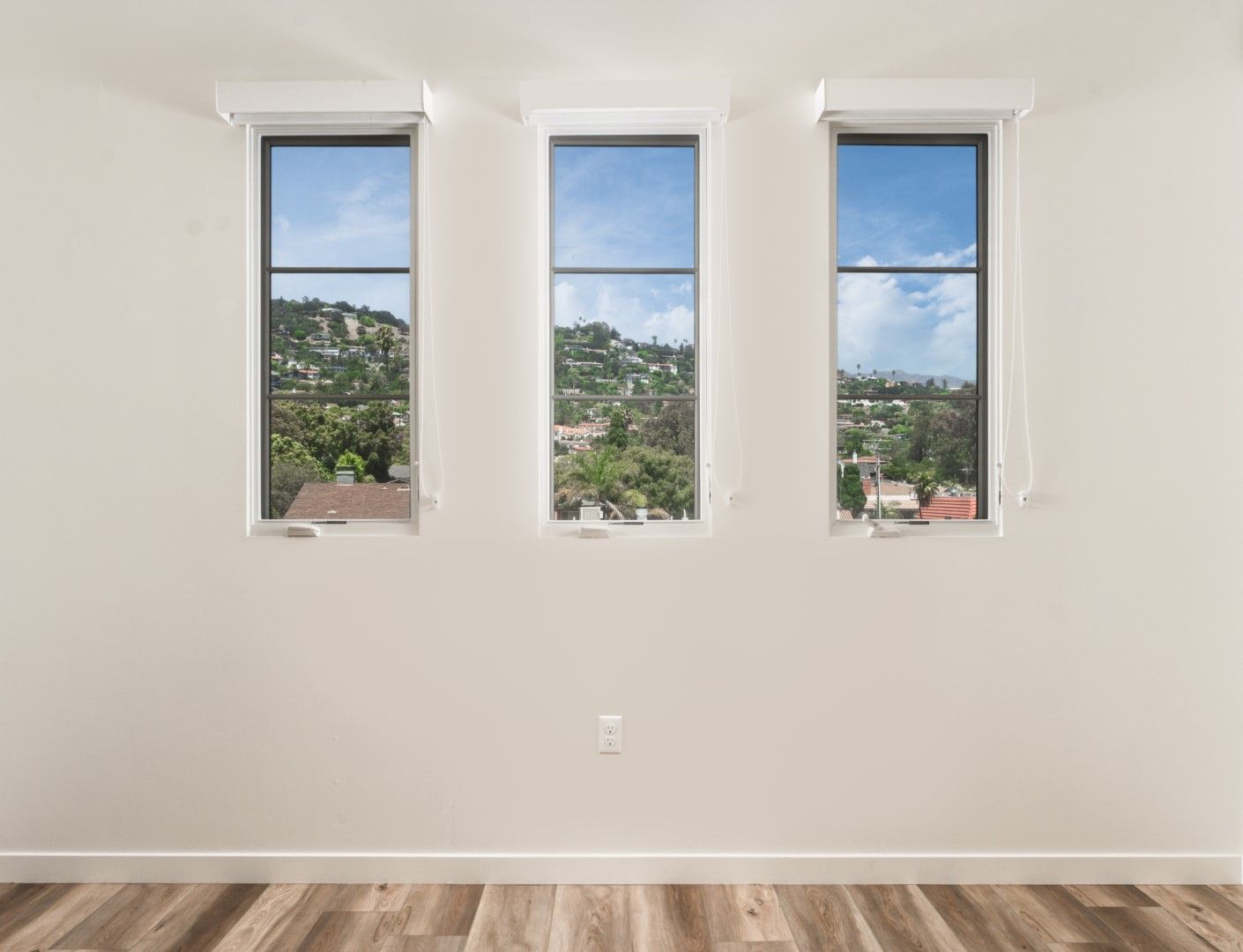 An empty room with three windows and a wooden floor.