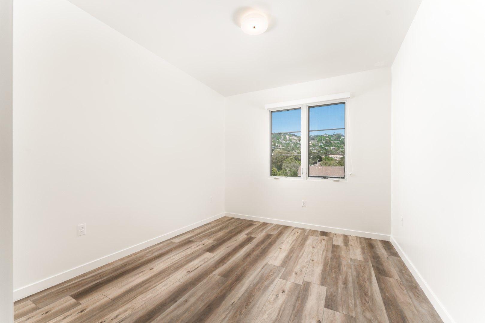 An empty bedroom with hardwood floors and two windows.