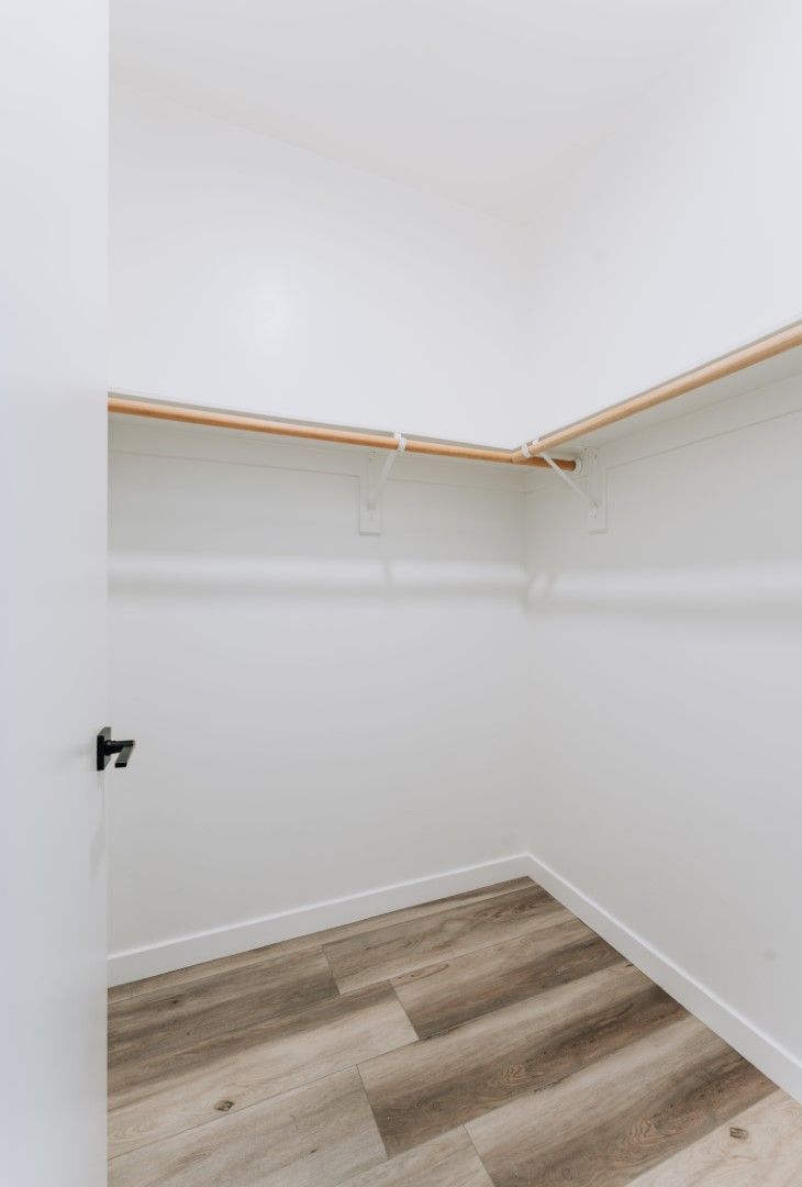 An empty walk in closet with wooden floors and white walls.