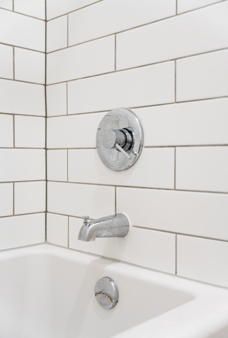 A bathtub in a bathroom with white tiles and a chrome faucet